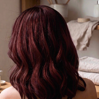 Medium-length wavy hair in a deep burgundy auburn shade, shown from behind on a person in a softly lit indoor setting.