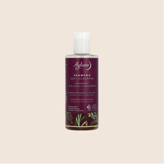 A bottle of Ayluna Shampoo with a white cap and a dark purple label featuring white text and botanical illustrations, centered on a light beige background.