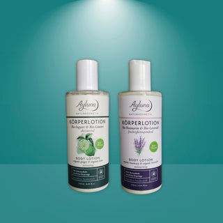 Two bottles of Ayluna Naturkosmetik body lotion, one with green and white labeling and one with purple and white labeling, set against a teal background with a spotlight effect.